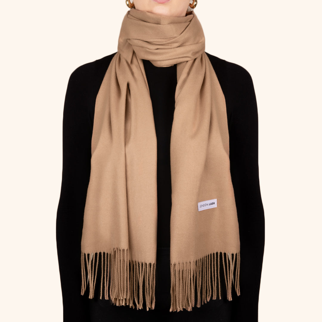 A person wearing a beige oversized wool scarf with fringes, wrapped around the neck and tied at the waist.